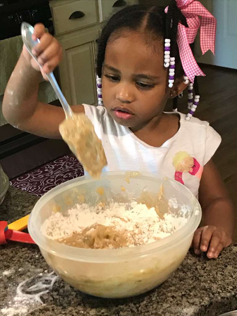 A young Little Risers student carefully mixing batter in a bowl