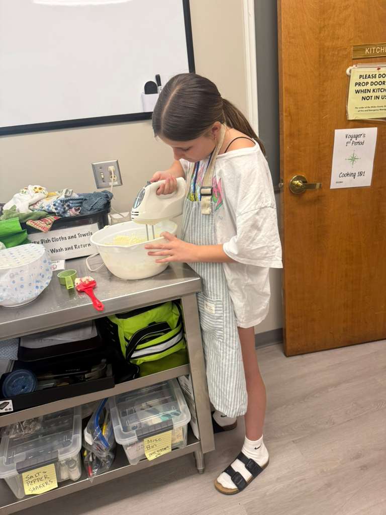 A Crown Builders teen using a hand mixer in a studio kitchen